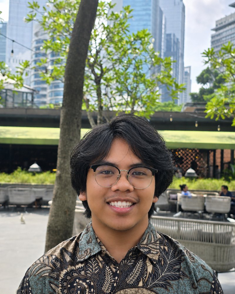 Foto Fasya Haikal, berkacamata dan memakai kemeja batik, tersenyum di area taman luar ruangan